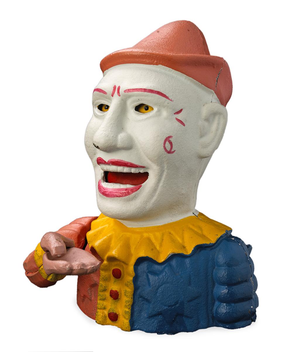 Clown en fer, visage blanc, maquillage coloré, main tenue sous une bouche ouverte.