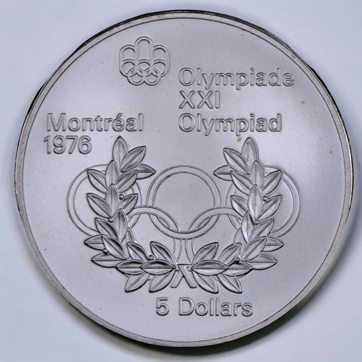 Pièce d’argent, symbole olympique de deux anneaux surmontés de trois anneaux liés, une couronne de feuilles de laurier est à l’avant-plan.