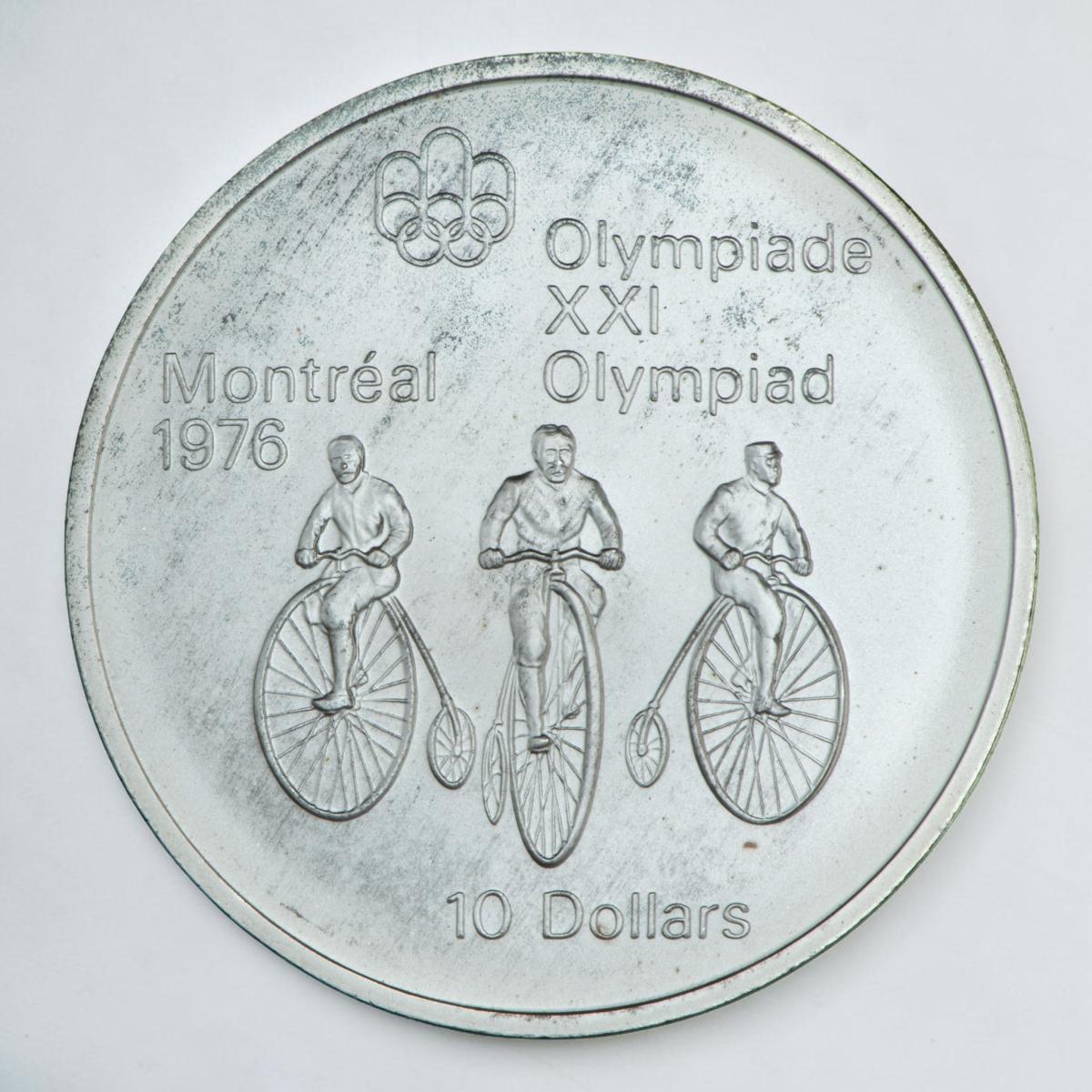 Pièce d’argent montrant de face trois hommes sur des vélos à grandes roues.