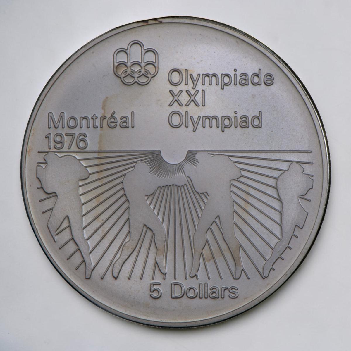 Pièce d’argent montrant des rayons de soleil sur la moitié inférieure et les silhouettes d’athlètes boxant avec des gants ronds.