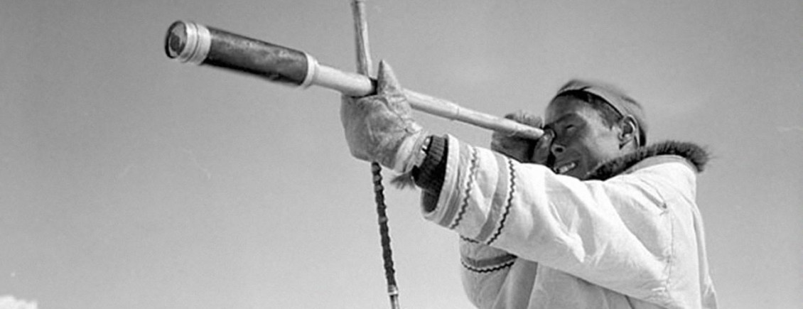 Photo en noir et blanc d’un chasseur inuit qui regarde dans une longue-vue.