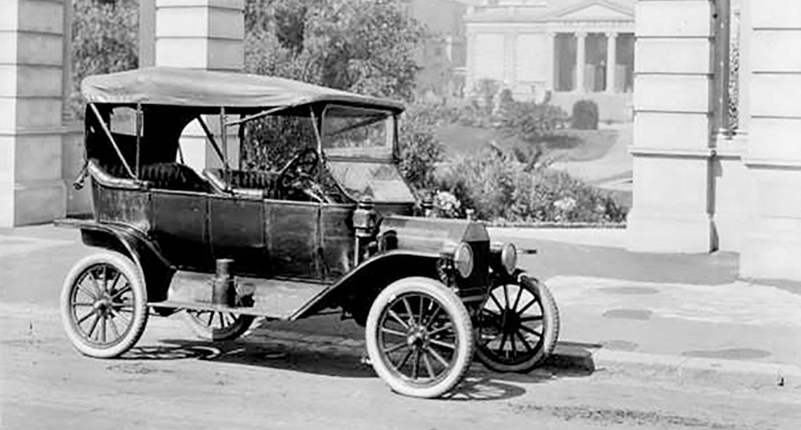 Photo historique d’une automobile stationnée devant des édifices publics avant la Première Guerre mondiale.