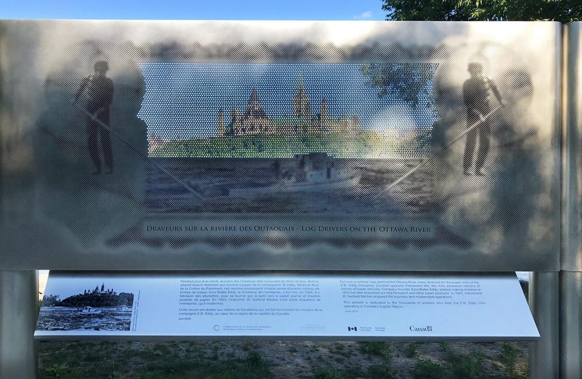 Photographie en couleurs d’un panneau en métal perforé sur lequel il y a une photo au travers de laquelle on peut voir le paysage. 