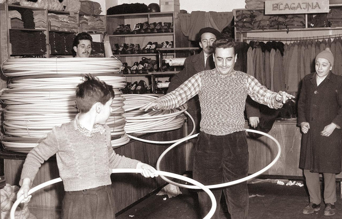 Photographie en noir et blanc d’un homme et d’un garçon faisant tournoyer de gros cerceaux autour de leurs hanches dans un magasin de vêtements.