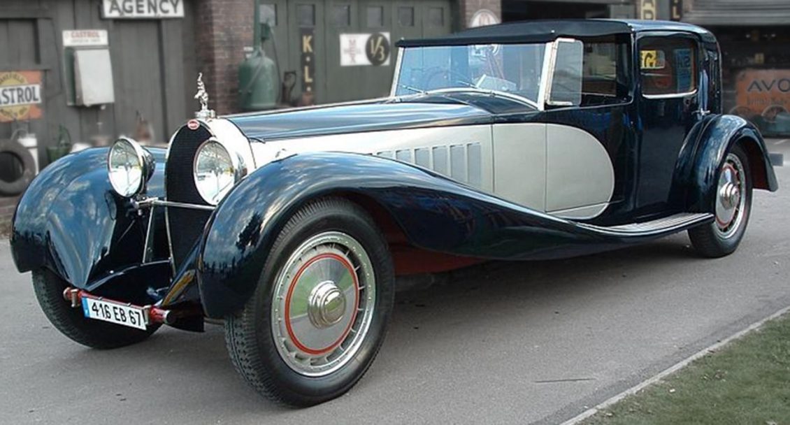 Photographie en couleur d’une longue voiture ancienne argent et noir.