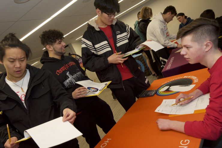 Un jeune assis à une table est consulté par d’autres jeunes debout qui tiennent une tablette.