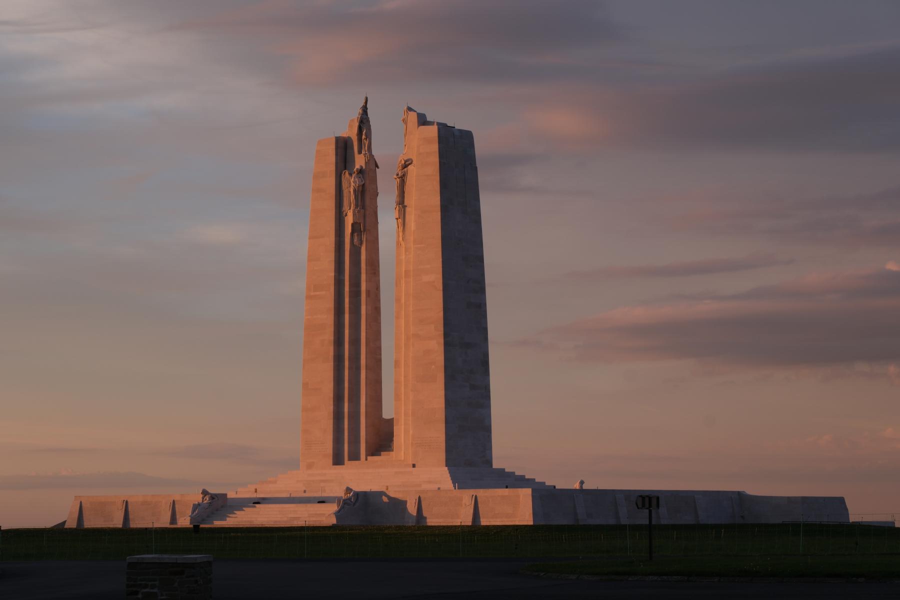 Mémorial de Vimy Photo du Mémorial national du Canada à Vimy, un imposant monument de pierre comprenant deux grands piliers et reposant sur une colline gazonnée, au coucher du soleil.